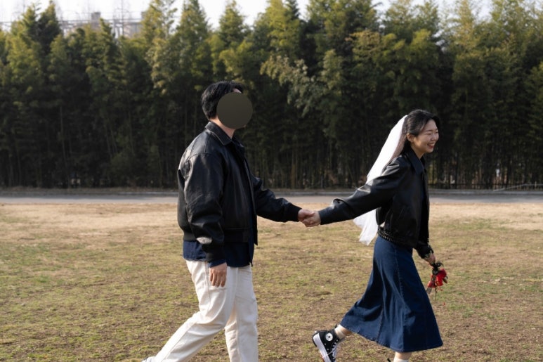 가죽 재킷에 데님 원피스와 베일을 매치한 신부가 신랑 손을 잡고 달려가는 초봄 공원 컷이에요.