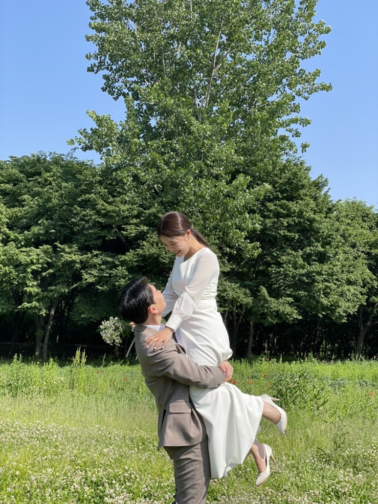 들판에서 신랑이 신부를 안아 올리는 컷