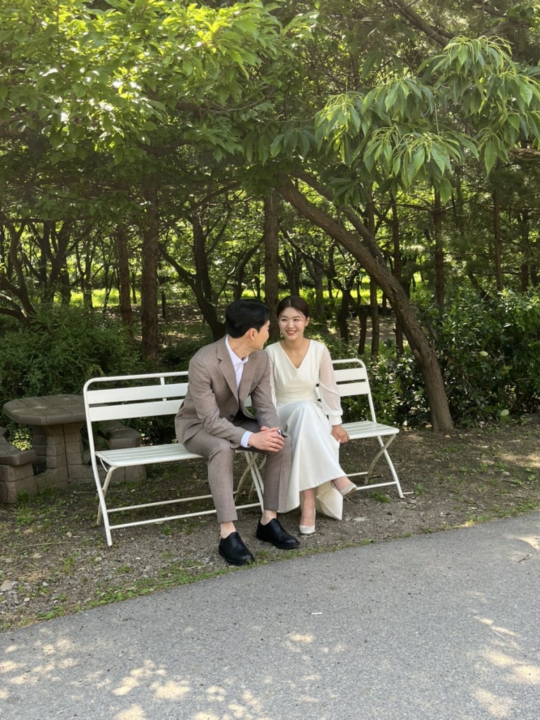나무 그늘 아래 흰 벤치에 나란히 앉은 컷