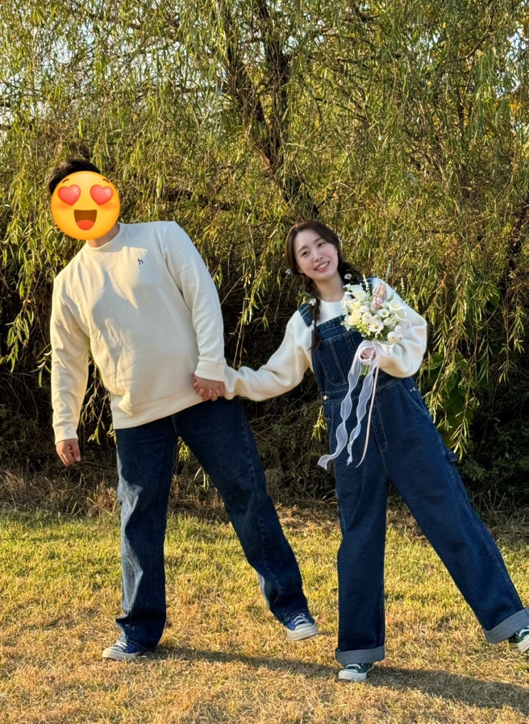 아이보리 니트에 청바지, 데님 멜빵바지로 맞춘 커플이 손잡고 장난스럽게 서 있는 컷이에요.