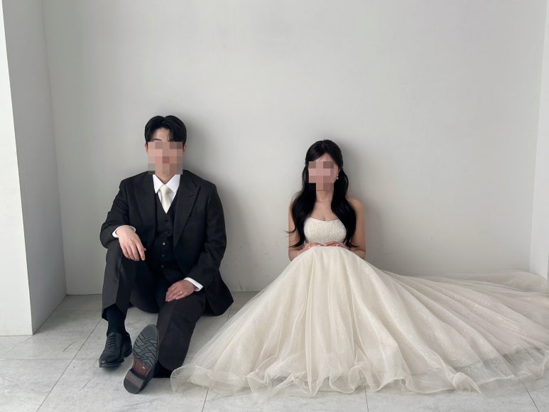 흰 벽 코너 바닥에 앉은 커플, 벽 전체가 보이는 넓은 컷