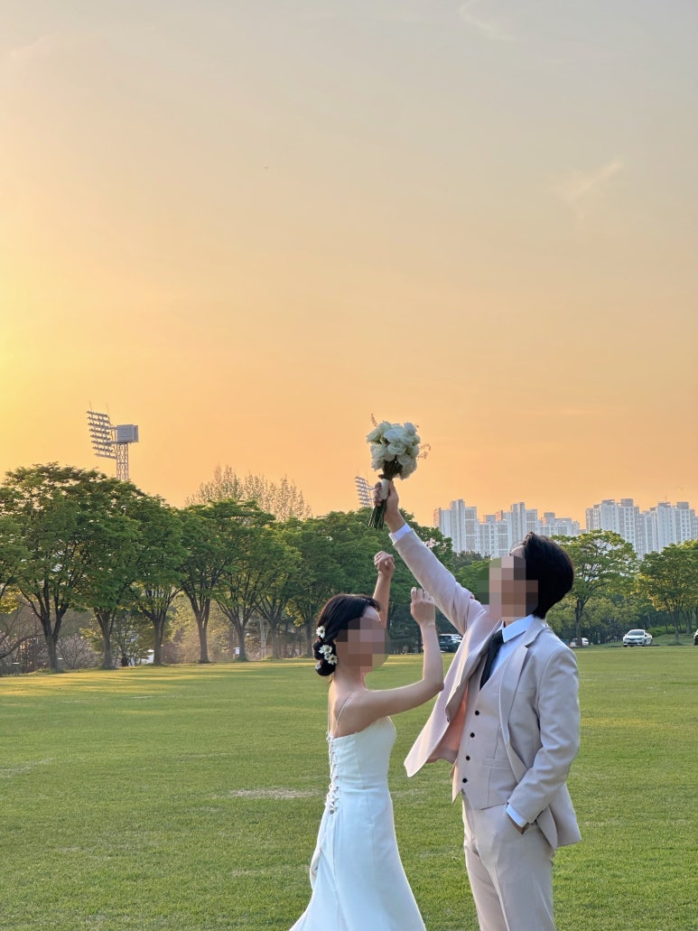 주황빛 노을 하늘 아래 부케를 들어 올리는 컷