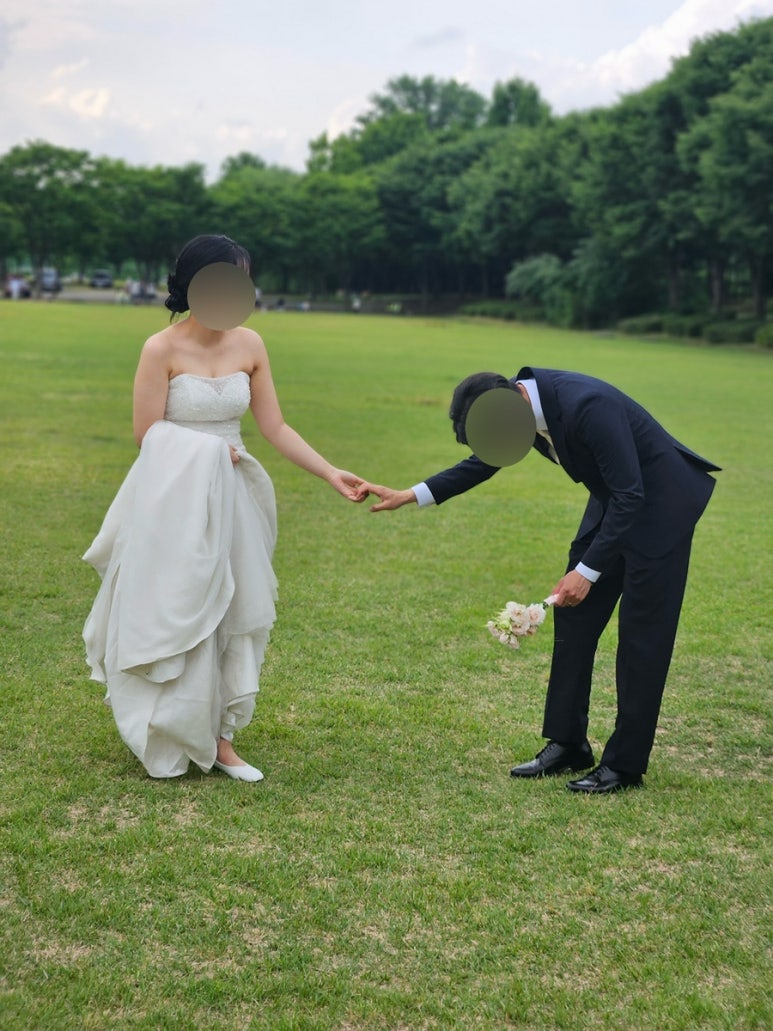 넓은 잔디밭에서 신랑이 허리 숙여 손잡는 컷, 뒤로 나무 라인