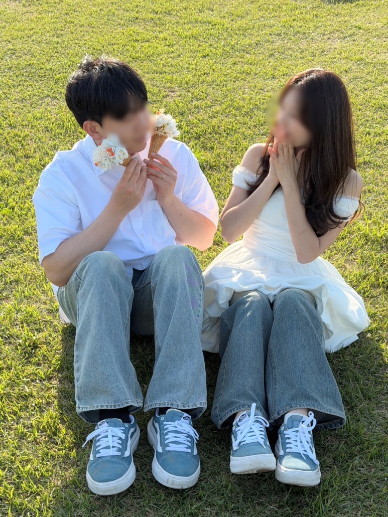 청바지 위에 흰 미니 드레스를 겹쳐 입은 신부와 신랑이 잔디에 앉아 아이스크림을 들고 웃는 아이폰 셀프 컷이에요.