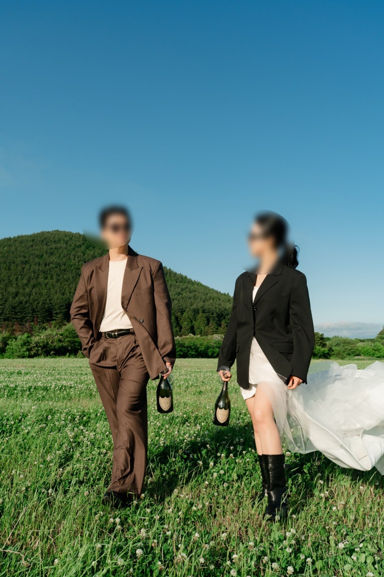 제주 들판을 걸으며 두 사람이 각자 샴페인 병을 한 병씩 들고 여유롭게 걸어요