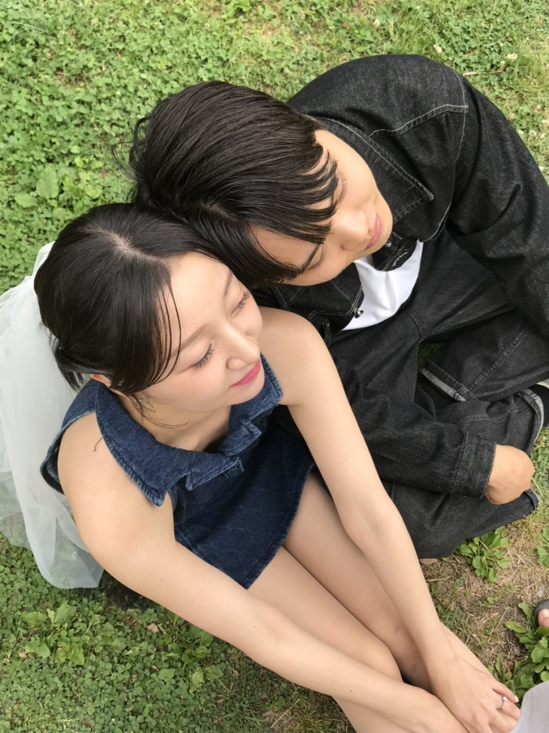 잔디 위에 기대앉아 신랑이 신부 어깨에 얼굴을 묻은 자연스러운 스킨십 컷이에요.