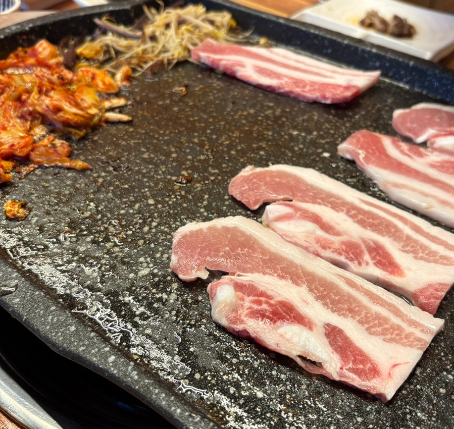달궈진 불판 위에 노릇하게 구워지고 있는 냉동삼겹살과 마늘