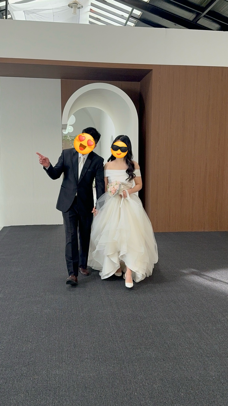 나무 벽 앞 흰 아치 통로를 걸어 나오는 커플