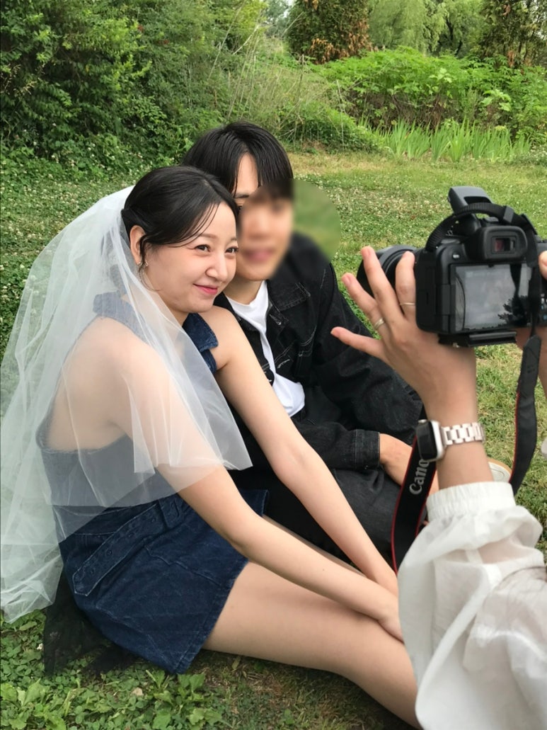데님 탑과 미니스커트에 베일을 쓴 신부와 블랙 데님 재킷의 신랑이 잔디에 앉아 웃는 컷이에요.