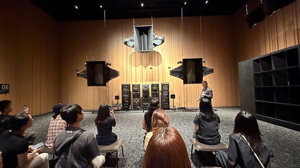 대형 극장용 음향 시스템을 마주 보는 청음 장면. 장비의 역사를 ‘보는 전시’와 실제로 ‘듣는 시간’이 교차한다.
