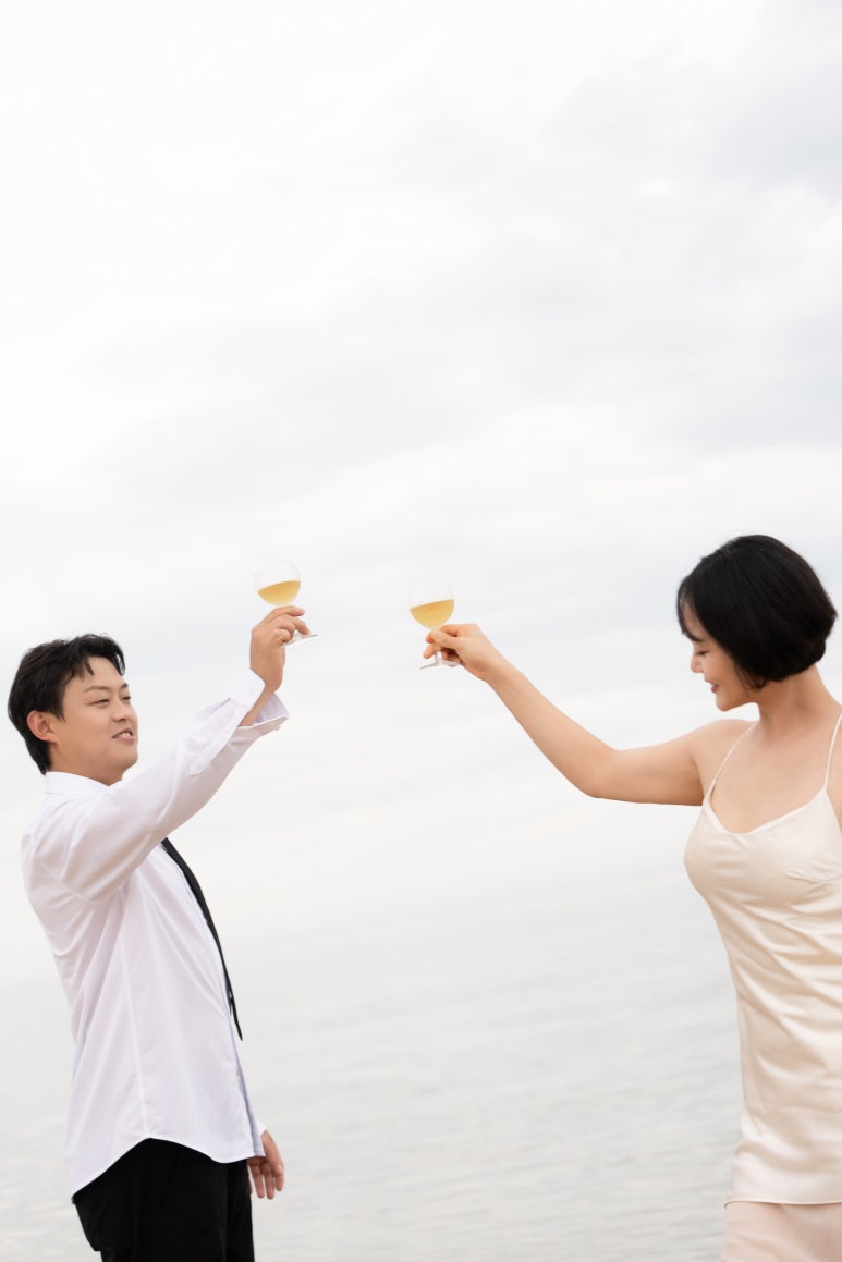 하얀 하늘을 배경으로 두 사람이 샴페인 잔을 높이 들어 건배해요