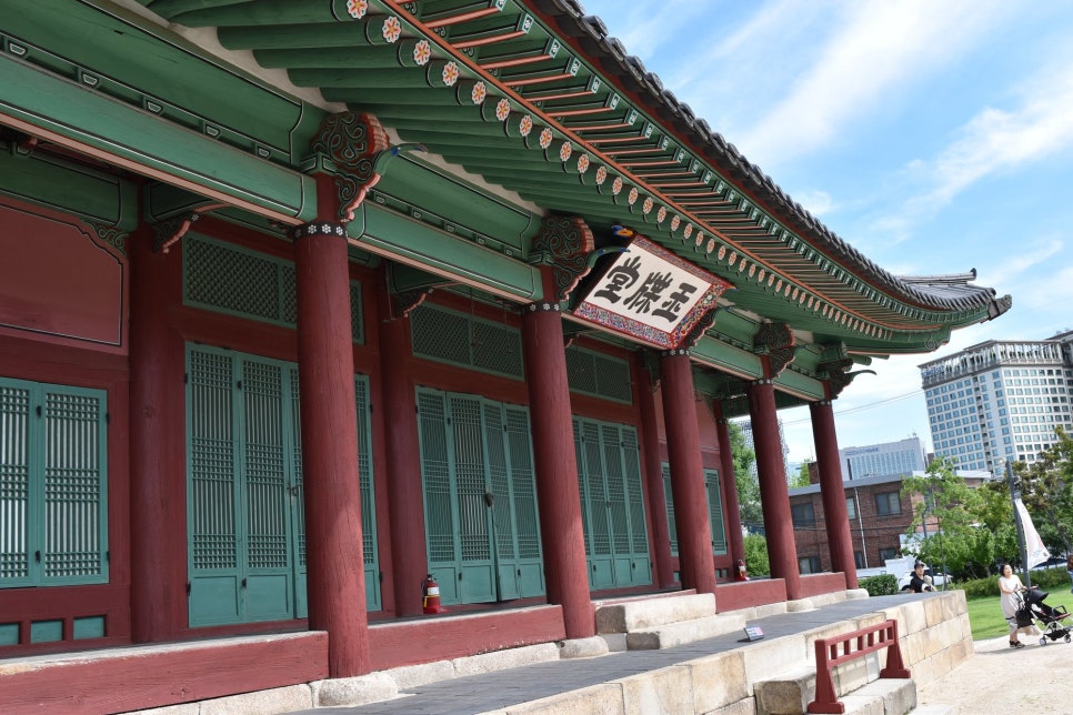 종친부 옥첩당의 단청 기둥 사이로 멀리 도심 고층 빌딩이 보이는 풍경