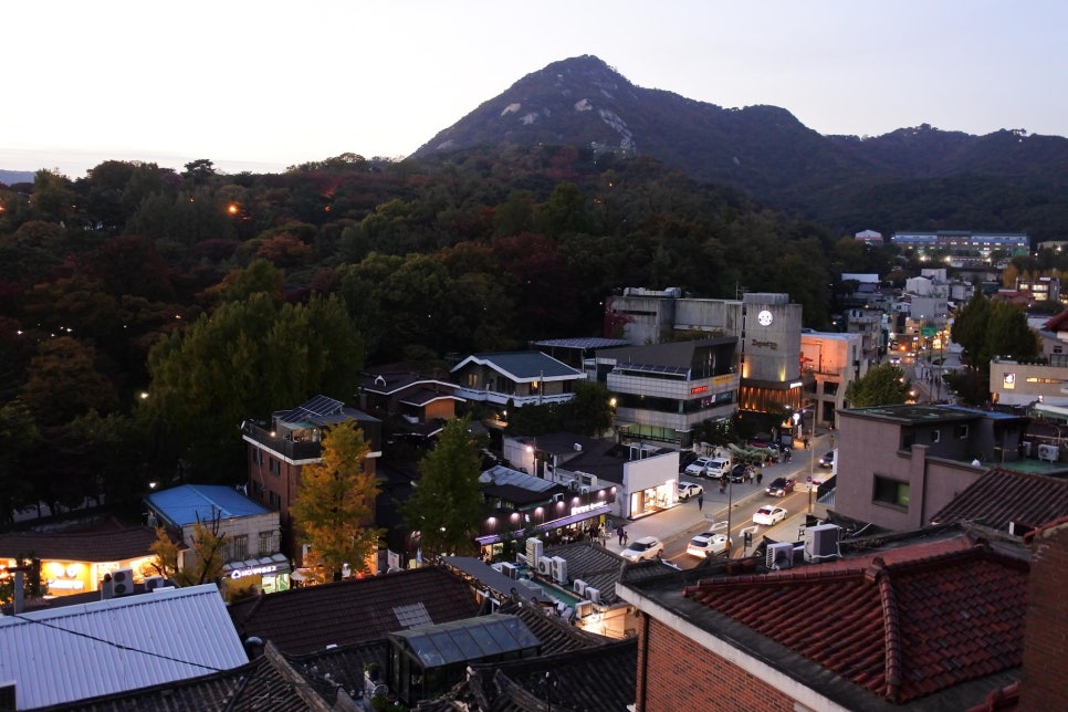 해질녘 삼청동 거리, 북악산 실루엣 아래 한옥 지붕과 상점 불빛이 보인다