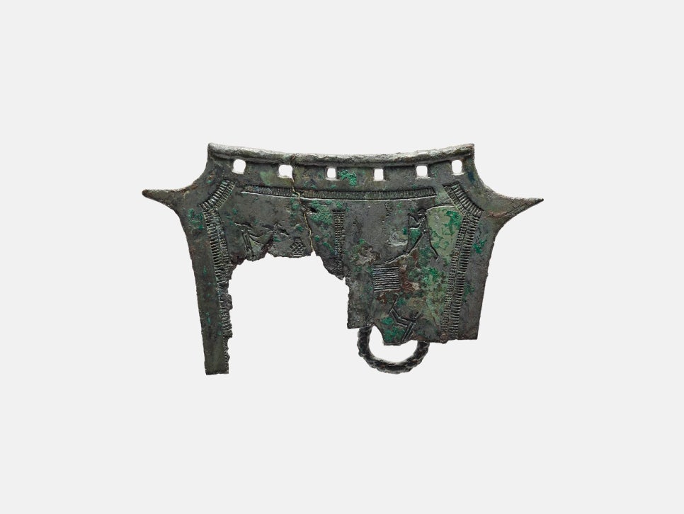 A shield-shaped bronze plate, only its upper part surviving, incised with a figure ploughing a field and another carrying a jar.