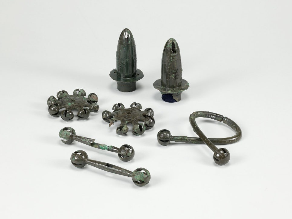 Several bronze rattles laid out side by side, one with eight arms and another with two.
