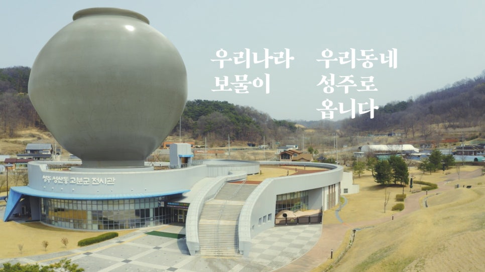 A promotional video still with a white porcelain moon jar composited at giant scale above the Seongsan-dong Tombs exhibition hall in Seongju.
