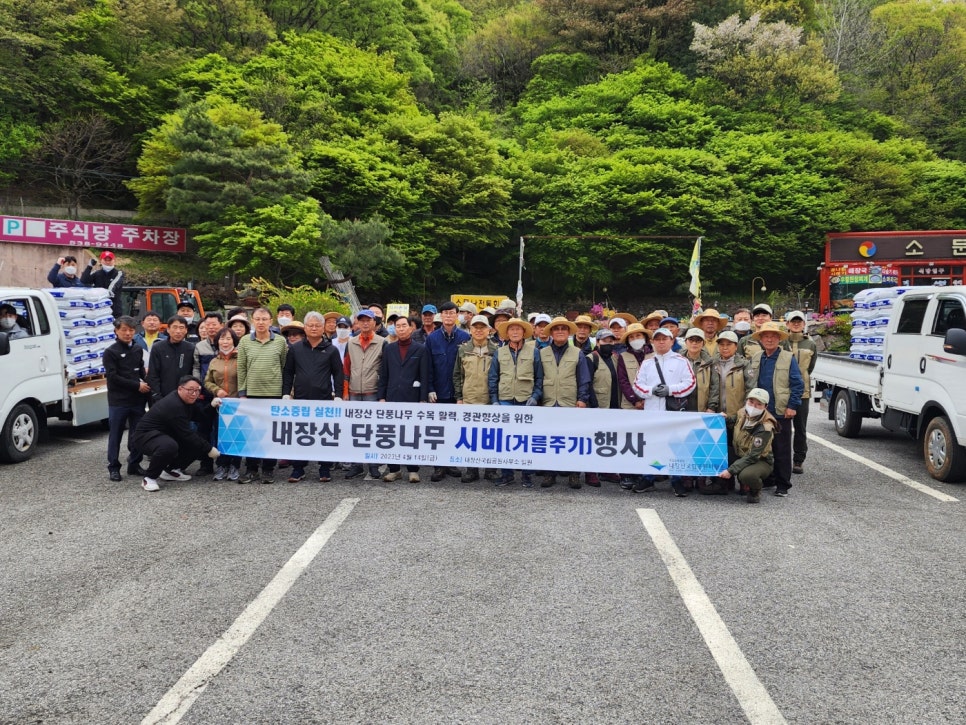 Volunteers and staff in a group photograph in front of a banner for the Naejangsan maple feeding event.