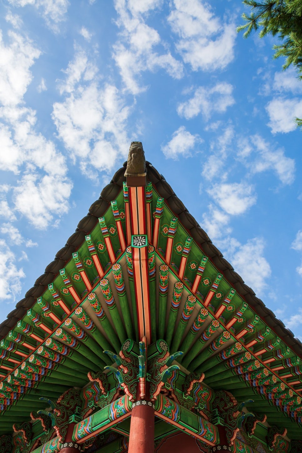 Looking up at a hanok's hip rafter and tiled roof, the courses of tiles and the eaves rafters visible.