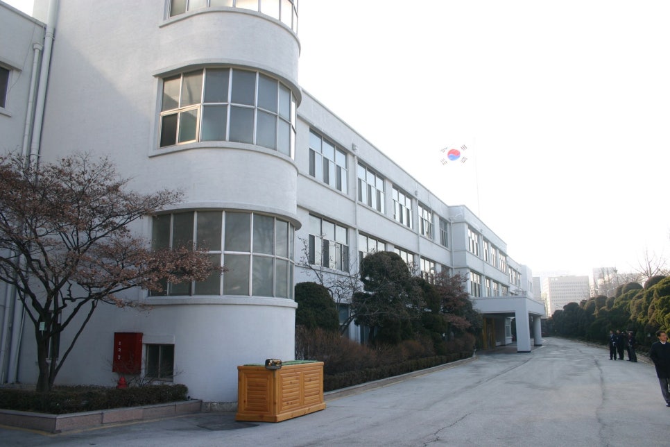 The side of the former headquarters building and the approach path towards the museum, brick-coloured walls and trees.