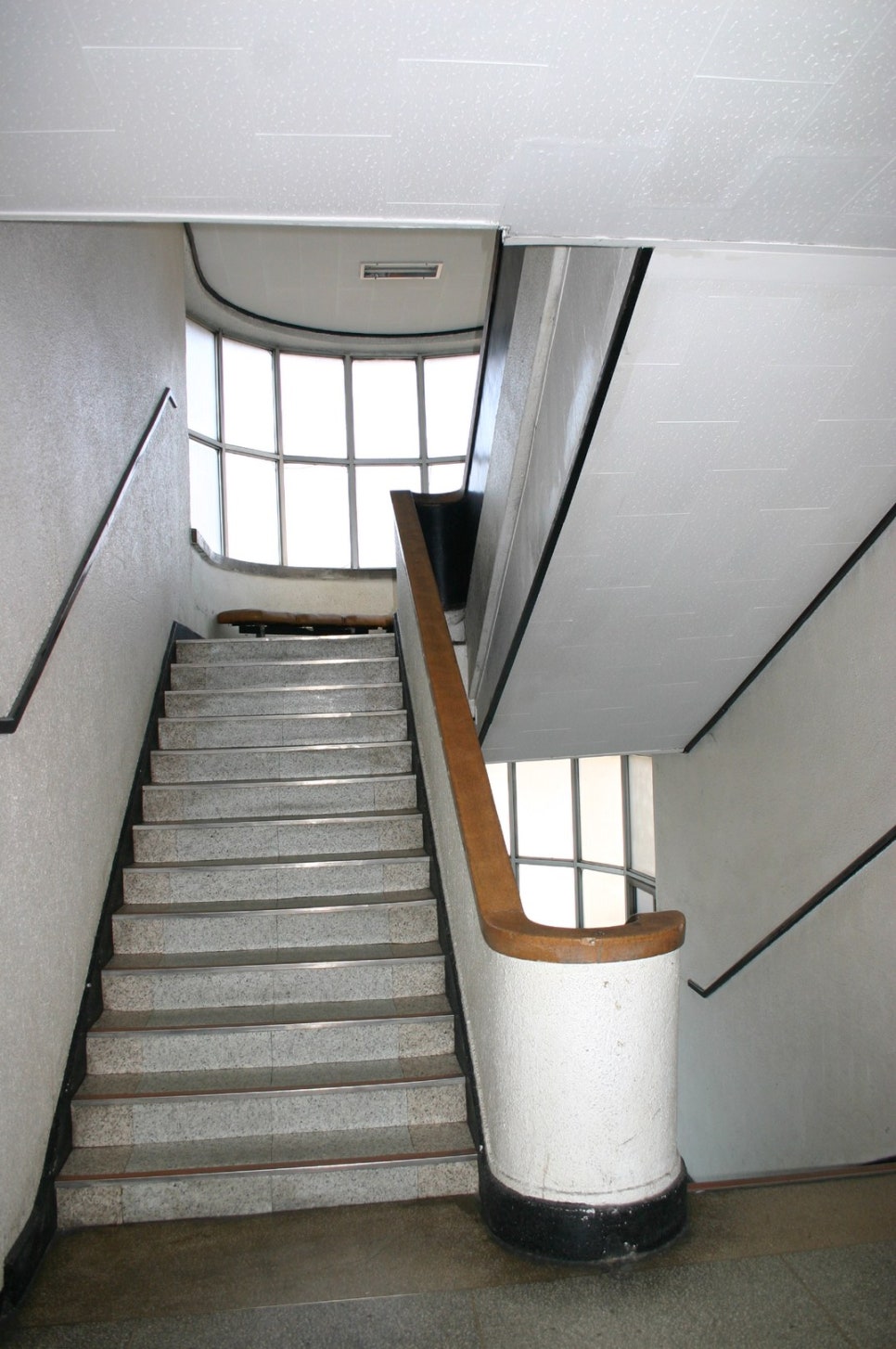 The curved stairwell inside the former headquarters building, the stairs turning in a half-circle up to the next floor along the balustrade.