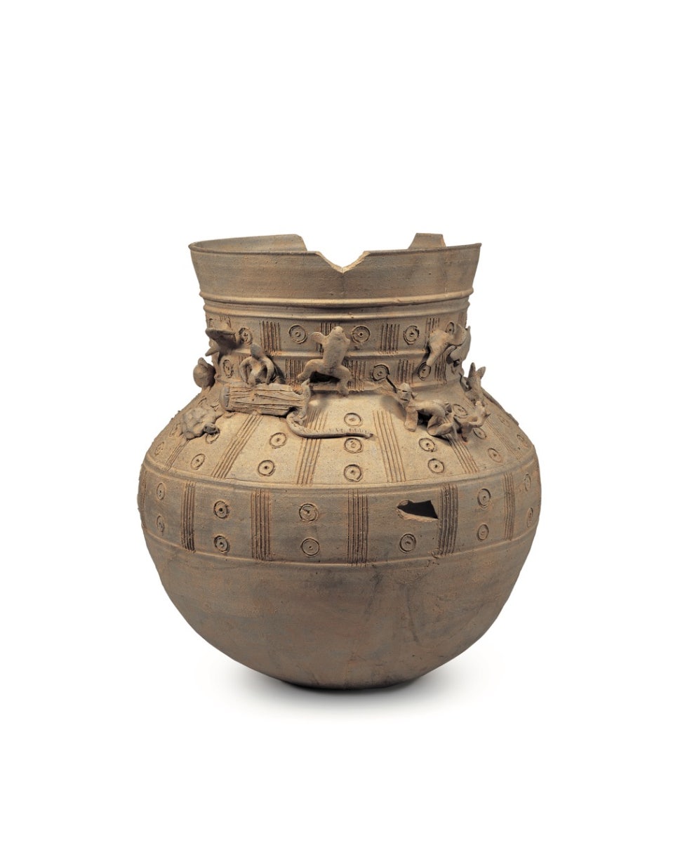 A grey long-necked earthenware jar with small clay figures of people and animals modelled onto its shoulder