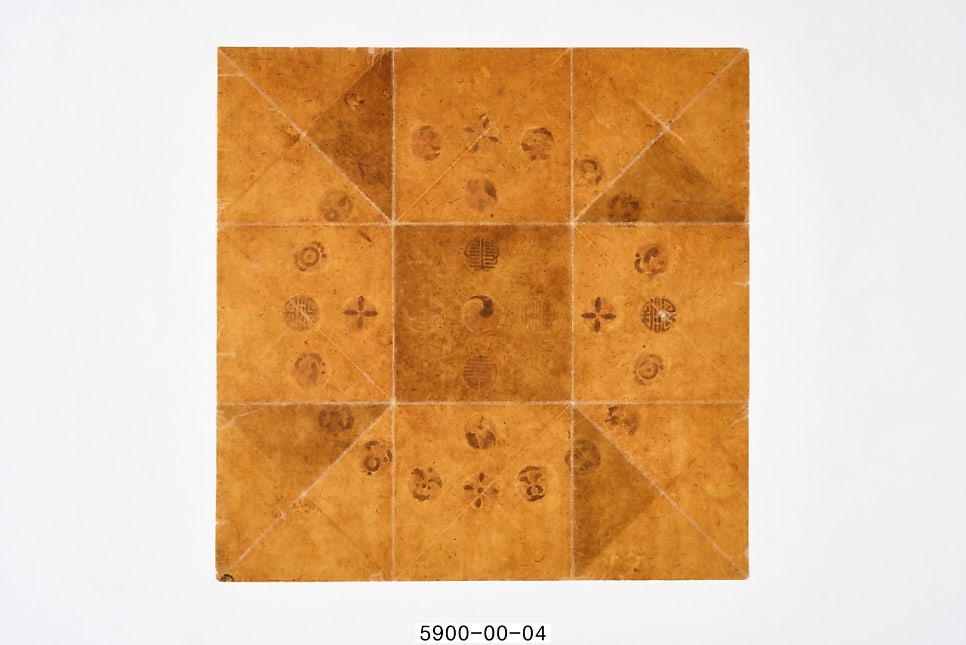 The reverse of the paper board. Grid-like fold lines cross the browned paper, along with faint blotches where the design on the front has pressed through
