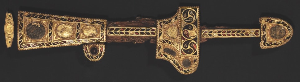A long horizontal gold-mounted dagger, its hilt and scabbard filled with gold ornament and set with red stones