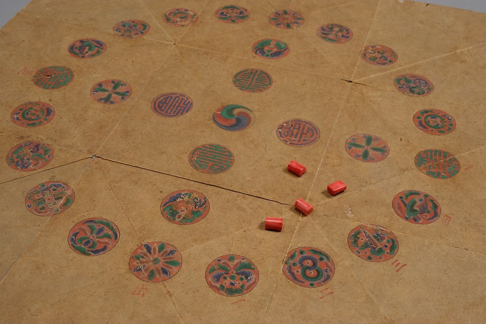The paper board photographed beside four very small yut sticks, each no longer than a finger joint