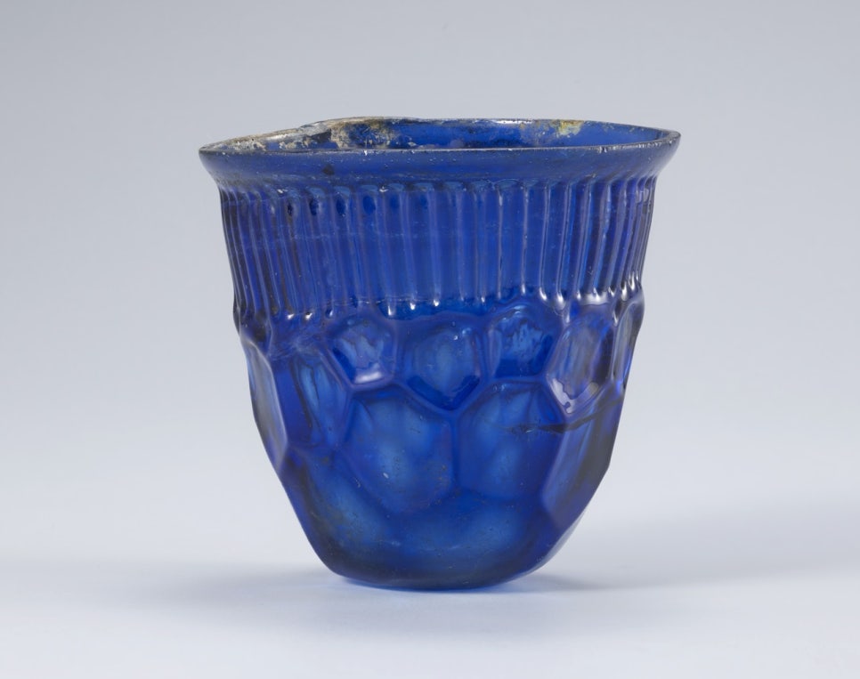 A pale blue-green glass cup, its surface regularly impressed with circular motifs