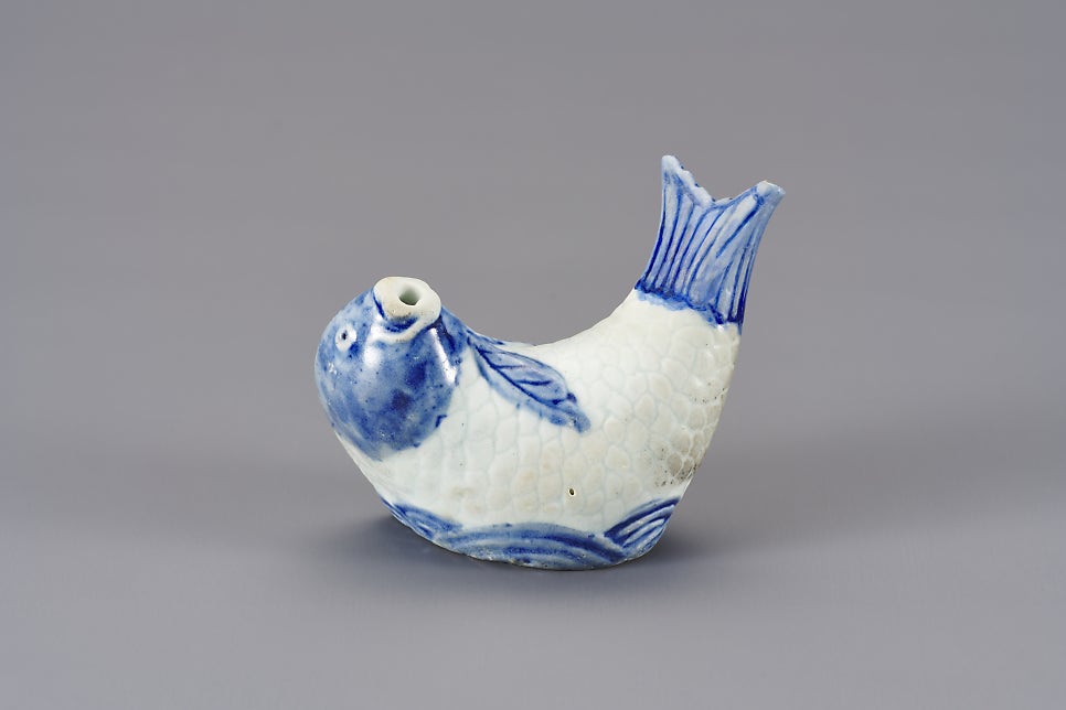A small white porcelain carp with its head dipped and tail fin raised, shown from the side
