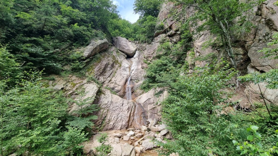 화강암 절벽 사이로 흰 물줄기가 흘러내리고 계곡 바닥에 바윗돌이 흩어져 있는 모습