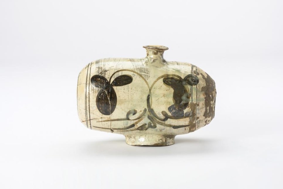 A buncheong jar shaped like an hourglass drum lying on its side, painted in iron with grass and flower motifs