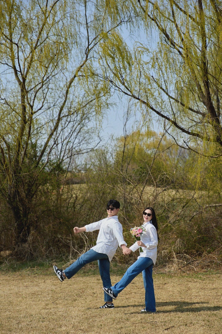선글라스를 쓴 커플이 손을 잡고 똑같이 한쪽 다리를 들어 올리는 발랄한 포즈예요.