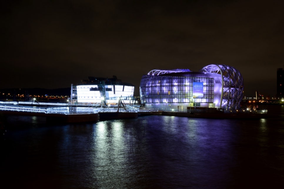 Floating Island buildings lit purple and blue, reflected in the river at night