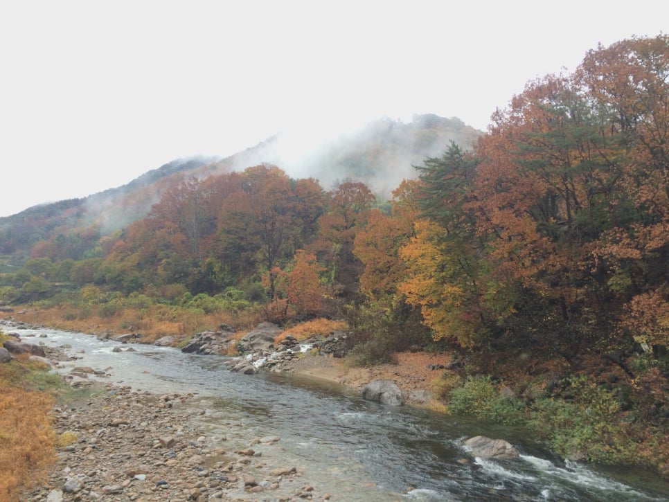 The Hwagae stream running between boulders under autumn hills, with a bridge
