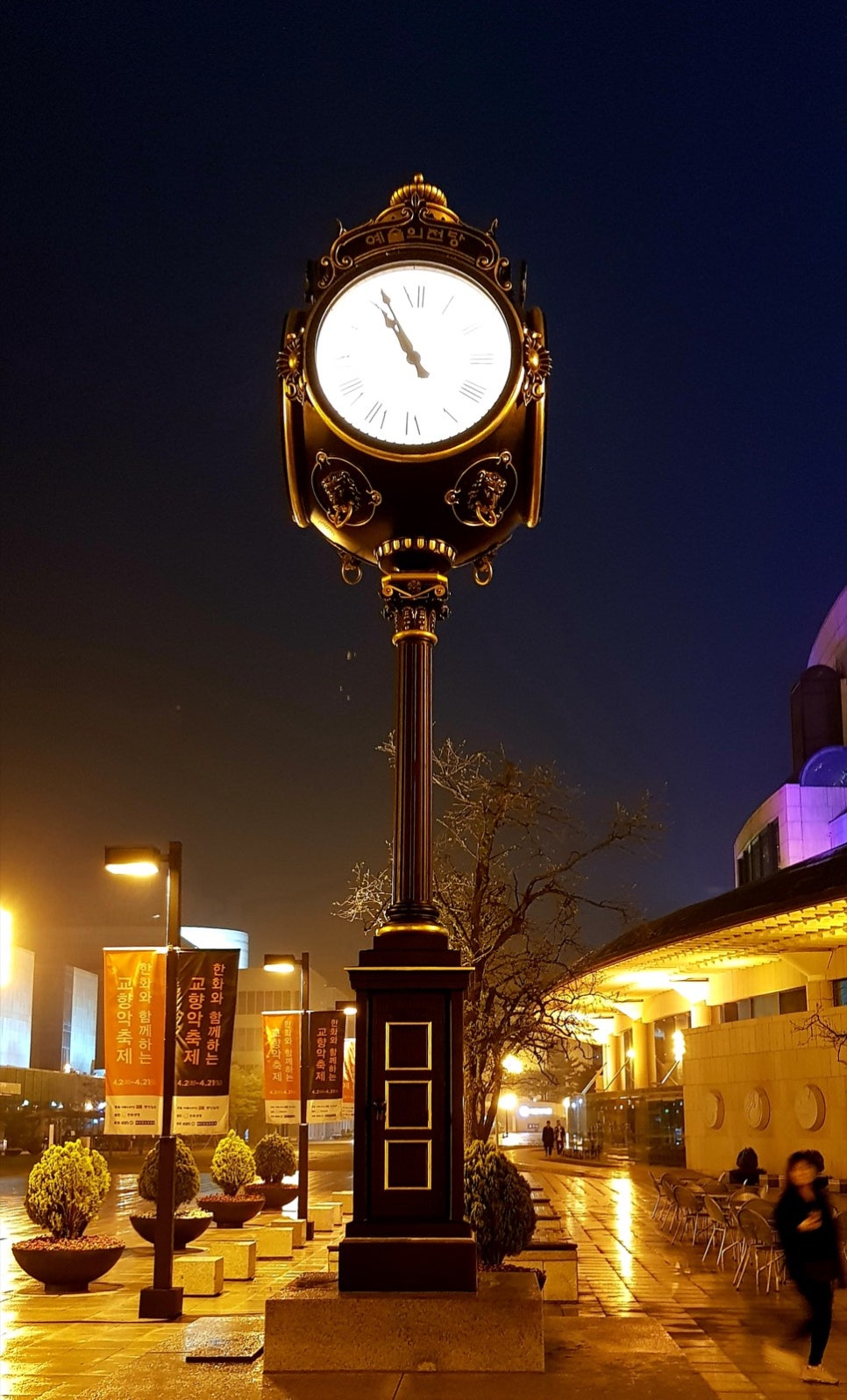 The illuminated clock tower and forecourt of Seoul Arts Center at night, in portrait format
