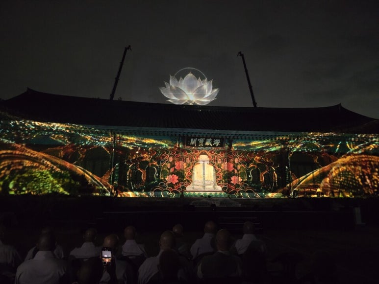 A lotus-shaped hologram floating in the night sky above the roof of Haejangbogak
