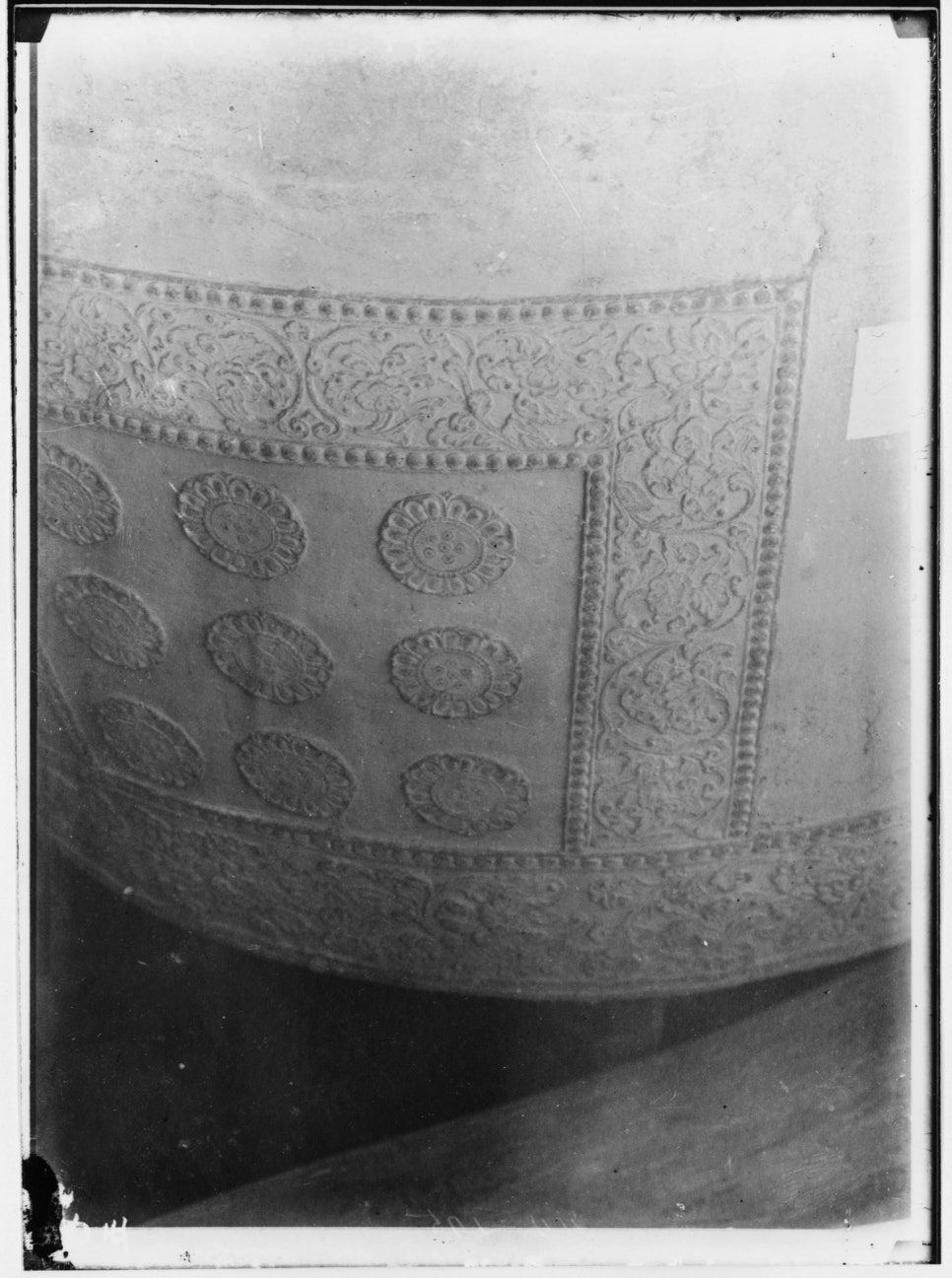 A square panel below the bell's shoulder holding nine raised lotus buds, with a band of scrollwork above it