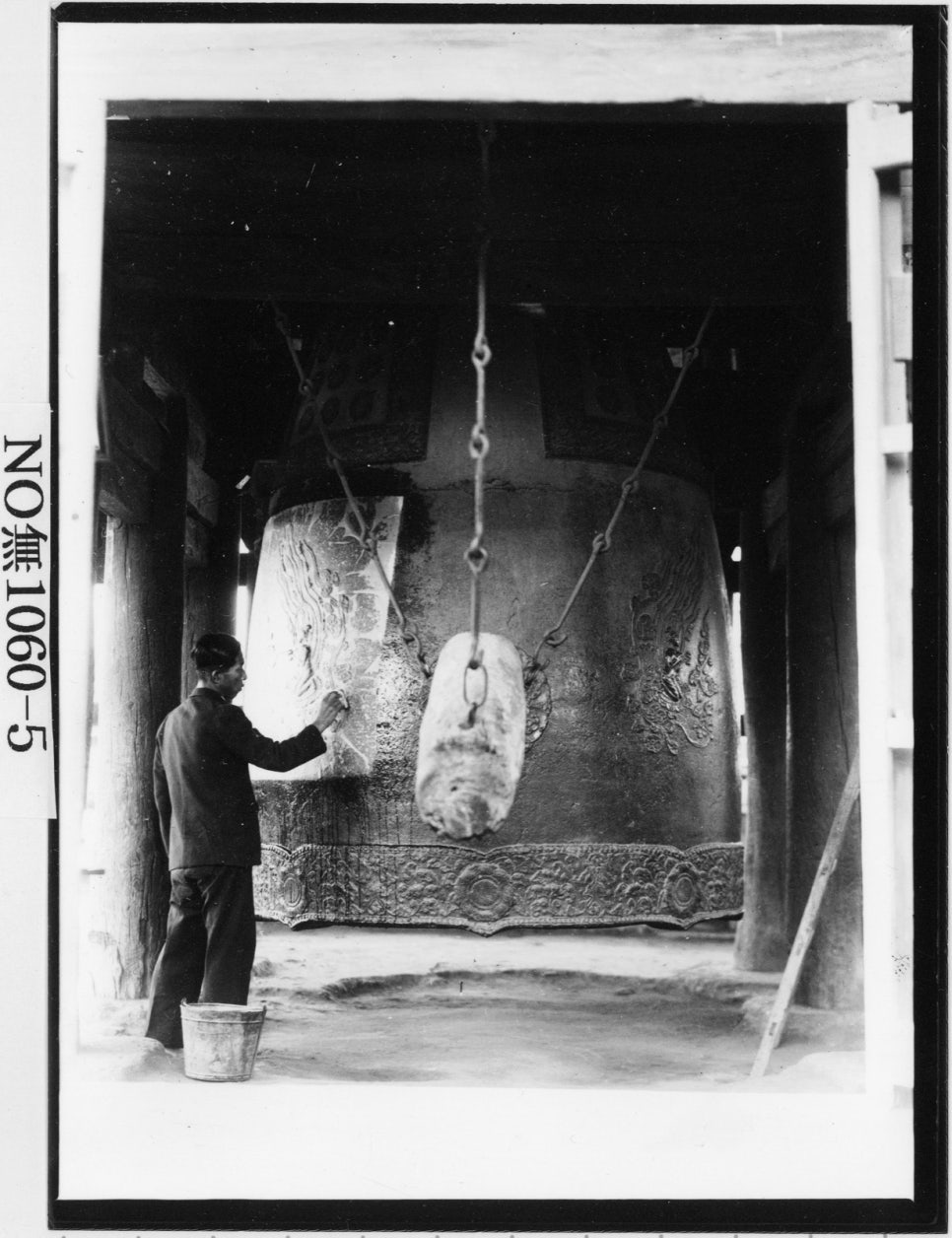 Black-and-white photograph of people standing at the bell and working on its surface, probably taking a rubbing
