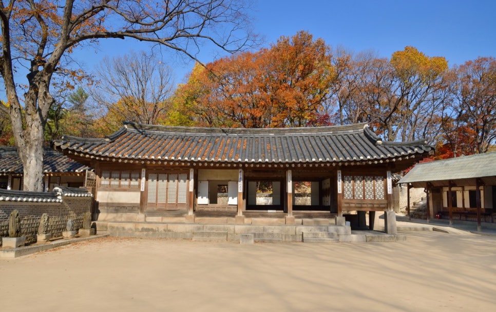 The unpainted men's quarters of Yeongyeongdang seen beyond red and yellow autumn trees