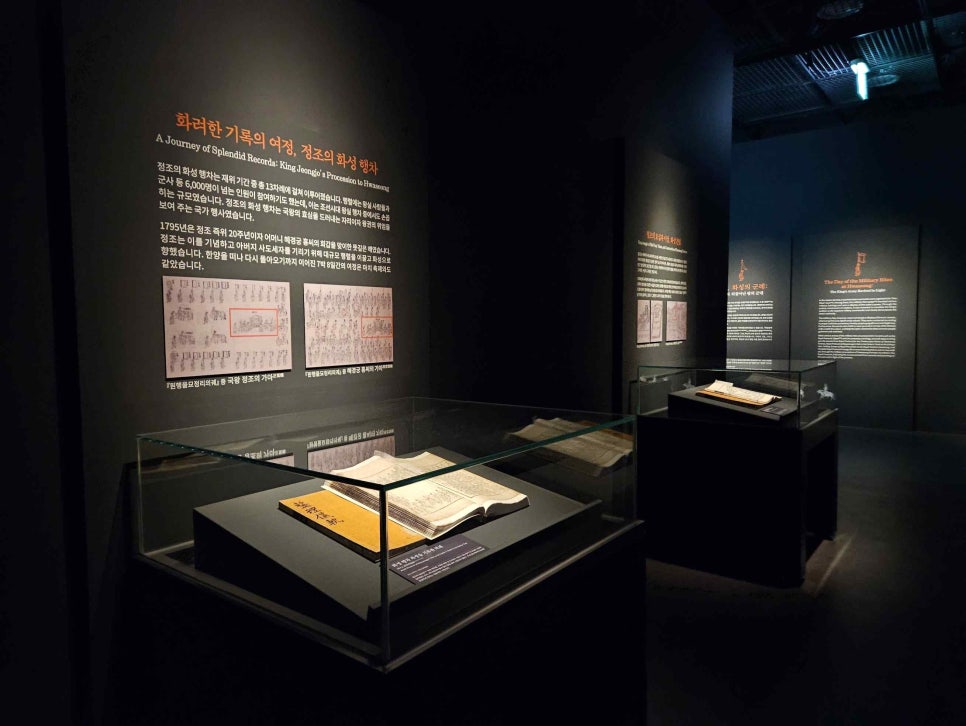 A dimly lit gallery interior with uigwe volumes open inside glass cases and explanatory panels on the wall