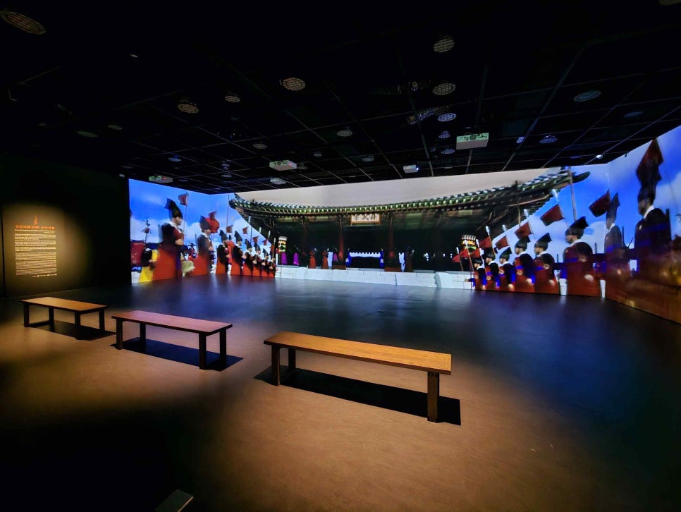 A darkened gallery with a wide panoramic screen showing palace buildings and a column of soldiers carrying banners
