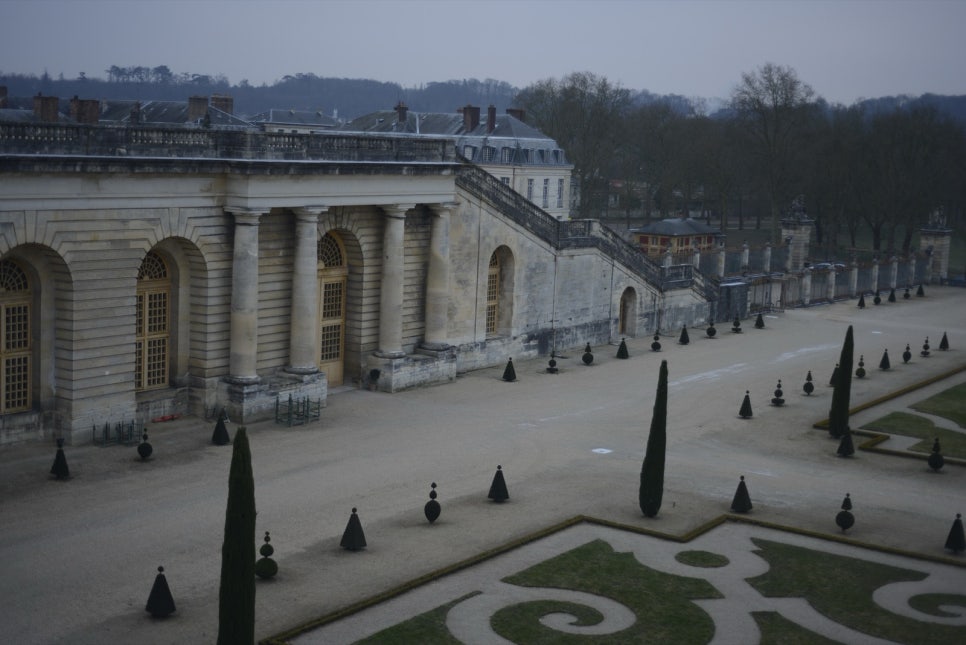 The Versailles orangery garden in winter, bare trees in front of a long stone building with a row of arched windows
