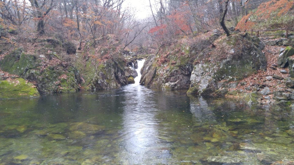 A small waterfall dropping into the dark pool of Guryongso in autumn rain