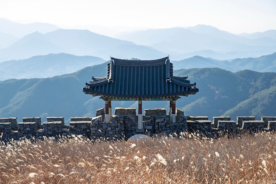 안개 낀 능선 앞에 선 황매산 성곽 누각과 앞쪽의 억새