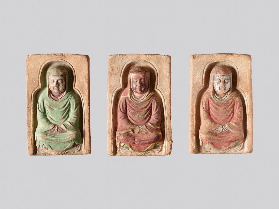 Three clay panels, each with a seated monk, placed side by side