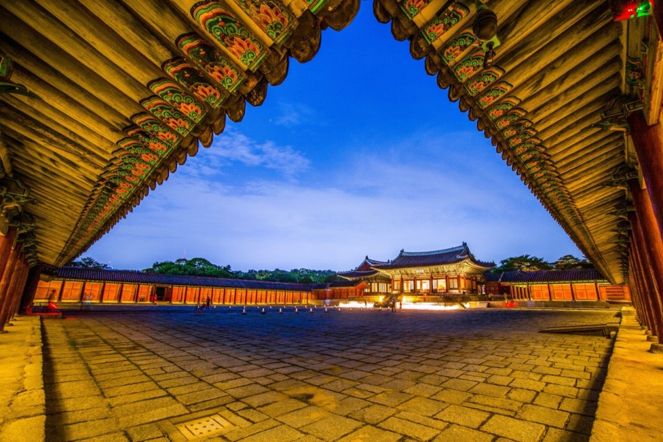 Myeongjeongjeon hall lit at night, seen past the eaves of the corridor