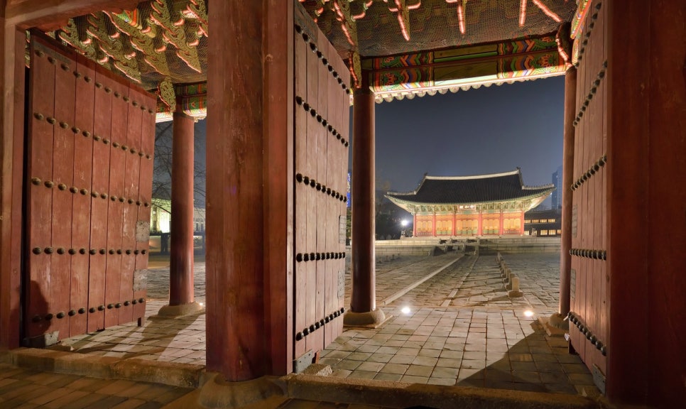 Junghwajeon hall at Deoksugung at night, its red columns and roof lit by floodlights