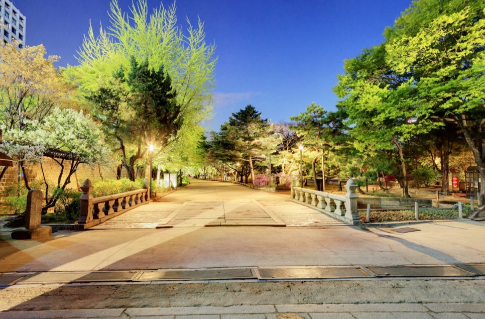 The stone Geumcheongyo bridge at Deoksugung and the trees around it under evening lights