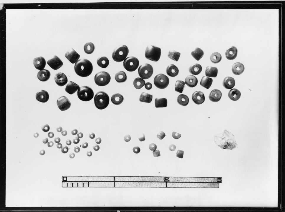 Black-and-white glass plate photograph of small glass beads laid out after excavation